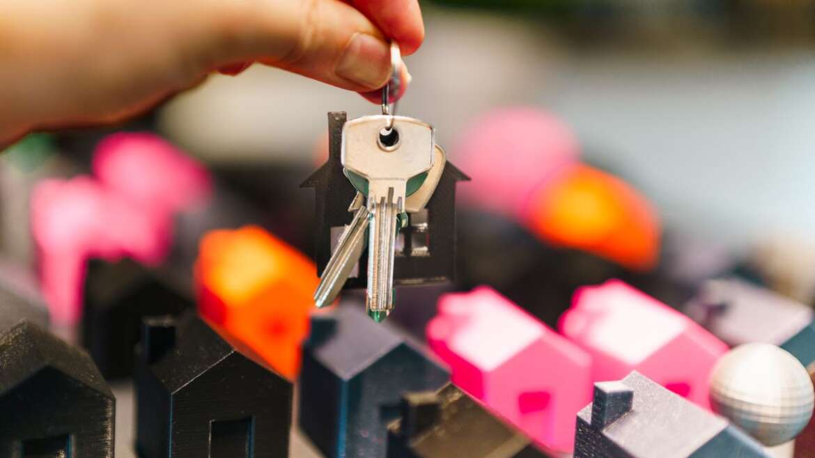 Molho de chaves suspenso sobre miniaturas de casas, representando o imóvel da herança ocupado por um único herdeiro.