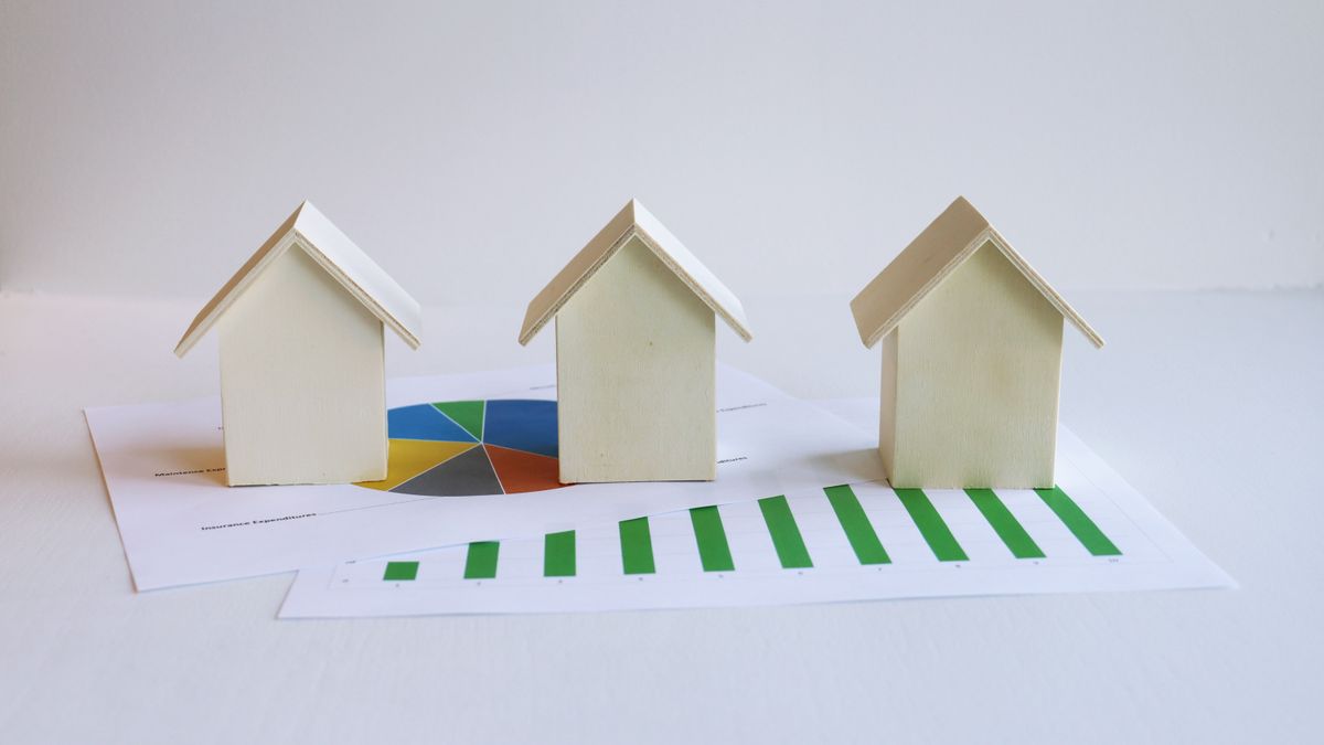 Miniaturas de casas sobre um gráfico impresso, representando a venda de imóvel entre pai e filho.