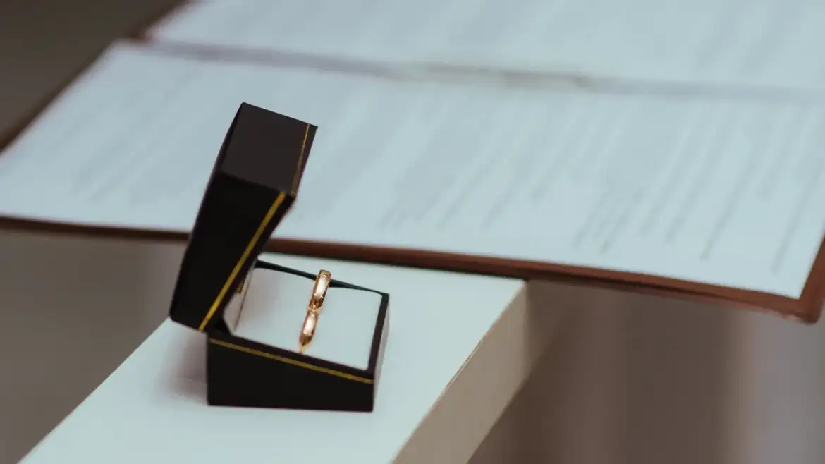 Aliança de casamento em estojo ao lado de documentos sobre uma mesa