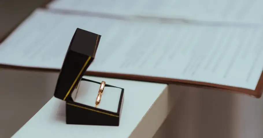 Aliança de casamento em estojo ao lado de documentos sobre uma mesa